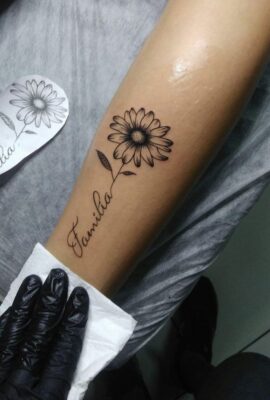 tattoo hoa hướng dương mực đen và chữ Hình xăm hoa cúc và chữ "Familia" trên tay, phong cách blackwork, chi tiết rõ nét, ảnh chất lượng HD.