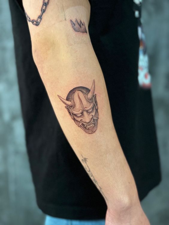 Hình xăm mặt nạ Oni trên cánh tay, phong cách blackwork, chi tiết sắc nét, ảnh độ phân giải HD.