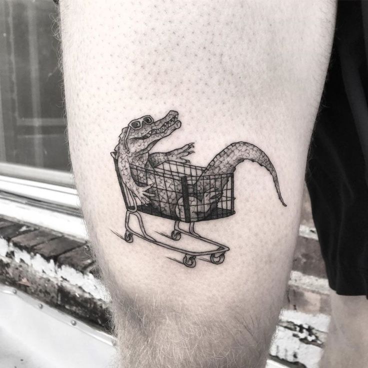 Hình xăm cá sấu ngồi xe đẩy trên đùi, phong cách blackwork, chi tiết rõ nét, độ phân giải HD.