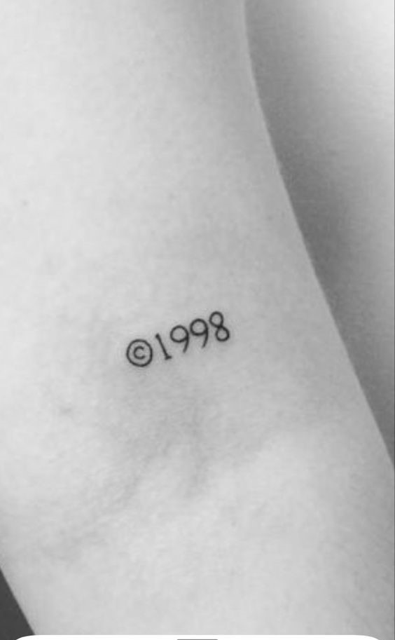 Hình xăm chữ "©1998" trên cánh tay, phong cách blackwork, ảnh chất lượng HD.